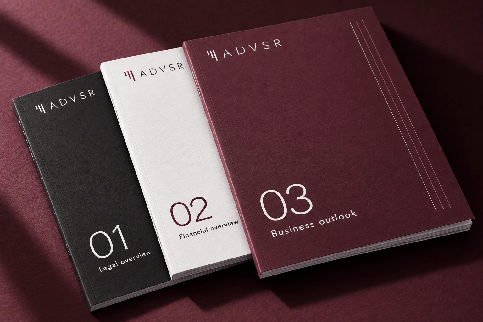 Three ADVSR document covers in graphite, white and wine.