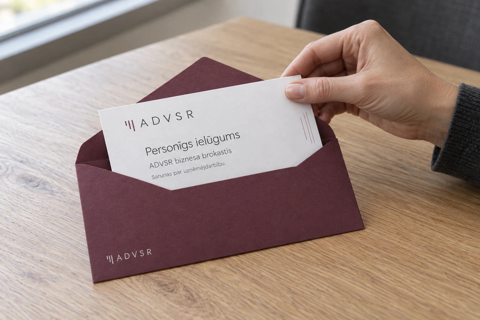 A hand takes an ADVSR business breakfast invitation out of a wine-coloured envelope.